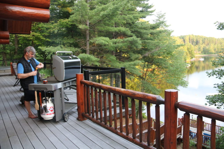 man barbequing on cottage deck with lake in background